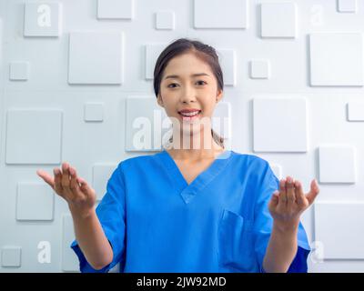 Porträt einer freundlichen, fröhlichen, lächelnden selbstbewussten asiatischen Frau Arzt oder Krankenschwester tun erklärende Geste mit ihren Händen auf weißem Hintergrund, Blick auf c Stockfoto