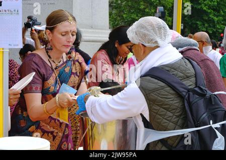 London, Großbritannien, 4.. September 2022. Eine Frau wird nach der Teilnahme an einer Wagenprozession von einem ehrenamtlichen Gaststättenhelfer vegetarisches Essen serviert. Hunderte von Hare Krishna-Anhängern tanzten und sangen neben einem riesigen Wagen, der von Dutzenden von Menschen mit Seilen gezogen wurde. Die Feierlichkeiten wurden am Trafalgar Square fortgesetzt, wo die Gäste die Aufführungen genossen haben. Kredit: Elfte Stunde Fotografie/Alamy Live Nachrichten Stockfoto