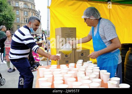 London, Großbritannien, 4.. September 2022. Ein Freiwilliger gießt einem Gast ein Fruchtgetränk, nachdem der Rathayatra-Wagenzug beendet wurde. Hunderte von Hare Krishna-Anhängern tanzten und sangen, während sie an einem riesigen Wagen entlang gehen, der von Seilen gezogen wird. Die Feierlichkeiten wurden am Trafalgar Square fortgesetzt, wo die Gäste die Aufführungen genossen haben. Kredit: Elfte Stunde Fotografie/Alamy Live Nachrichten Stockfoto