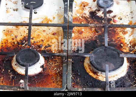 Schmutzige Oberfläche des Gaskofens. Vier Gasbrenner und ein gusseisernes Gitter eines Gasofens, umgeben von alten Essensresten und Getränken. Oberfläche des oberen Bereichs Stockfoto