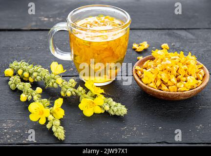 Kräutertee-Getränk aus Verbascum thapsus, der großen Königskerze, der Großen Königskerze oder der gemeinen Königskerze. Gelbe getrocknete Blütenblätter. Glasbecher. Stockfoto