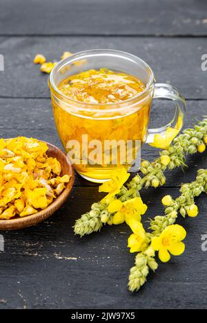 Kräutertee-Getränk aus Verbascum thapsus, der großen Königskerze, der Großen Königskerze oder der gemeinen Königskerze. Gelbe getrocknete Blütenblätter. Glasbecher. Stockfoto