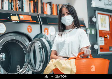 Ein brünett weißes Mädchen, das die Wäsche macht und einen orangefarbenen Wäschekorb in den Händen hält Stockfoto