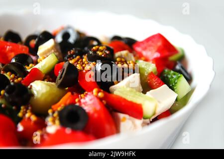 Sommersalat mit Nahaufnahme defokussieren. Klassischer griechischer Salat aus Tomaten, Gurken, rotem Pfeffer, Zwiebeln mit Oliven, Orangen und Feta. Frisches gemischtes Gemüse Stockfoto