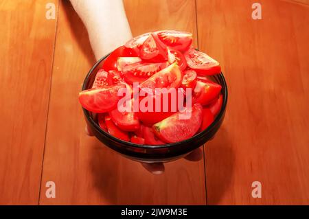 Eine Schüssel mit reifen roten, frisch gewaschenen, in Scheiben geschnittenen Tomaten in weiblicher Hand. Stockfoto