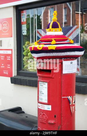 Skurrile bunte handgemachte gestrickte Wollmütze ziert eine traditionelle rote Säulenbox, die das Platin-Jubiläum von Königin Elizabeth II. Feiert England. Stockfoto