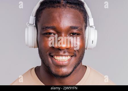 mexikanischer Mann mit weißem Kopfhörer, der Musik in beigefarbenem T-Shirt hört Stockfoto