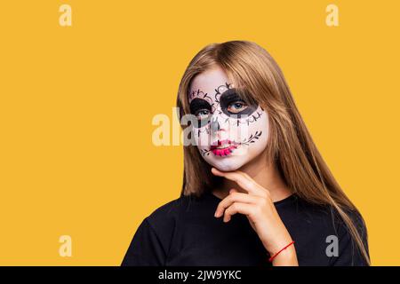 Teenager-Mädchen mit coolen Schädel Make-up mit Rosen auf dem Kopf Blick auf die Kamera in gelben Studio Stockfoto