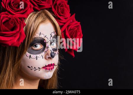 Portrait eines jungen schönen Mädchens mit Make-up Skelett auf ihrem Gesicht und roten Rosen auf dem Kopf Stockfoto
