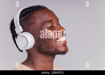 mexikanischer Mann mit weißem Kopfhörer, der Musik in beigefarbenem T-Shirt hört Stockfoto