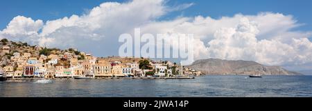 Panoramablick, Skyline der kleinen Oase der Insel Symi. Dorf mit winzigen Strand und bunten Häusern auf Felsen. Gipfel der Berge an der Küste von Rhodos, Dodekanes, Griechenland. Hochwertige Fotos Stockfoto