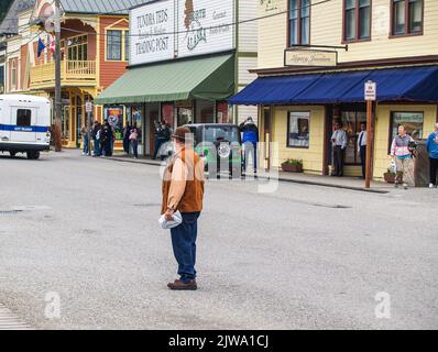 Skagway Alaska USA - Juli 31 2008: Ein Mann, der in der Straße steht und auf die Straße blickt, mit traditionellen Fassaden touristisch orientierter Gebäude im Hintergrund Stockfoto