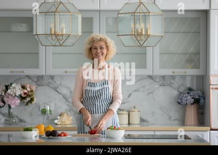 Happy mittleren Alters Kochen Blogger in Schürze Schneiden frisches Gemüse Stockfoto