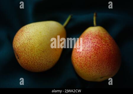 Zwei gelb-orange Birnen auf einem dunkelgrünen Tisch. Stockfoto