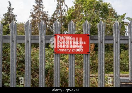 Rotes Warnschild mit der Aufschrift - Warnung Treten Sie nicht auf die Bahnstrafe £1000 an Metallzäunen neben der Eisenbahnlinie in Trowbridge, Wiltshire, Großbritannien Stockfoto