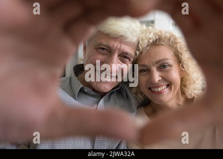 Glückliches Senior liebevolles Paar Porträt mit Hand herzförmigen Rahmen Stockfoto