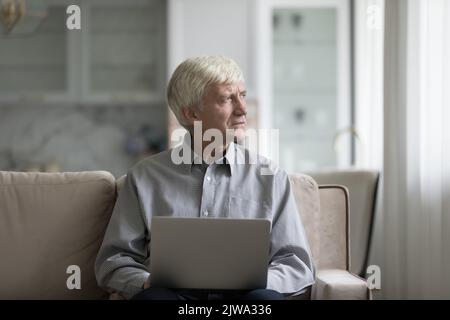 Nachdenklicher, fokussierter Rentner mit Laptop-Computer Stockfoto