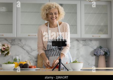 Fröhliche ältere Blogger im Ruhestand Frau Aufnahme Kochen Video Stockfoto