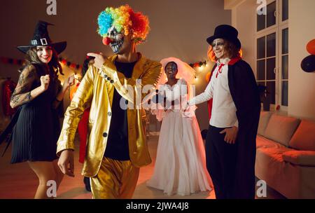 Fröhlicher selbstbewusster junger Mann im gruseligen Clown Kostüm, der Spaß auf der Halloween Party hat. Stockfoto