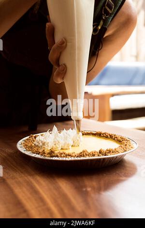 Frau, die einen Käsekuchen vorbereitet. Sie setzt Creme darauf, um ihr den letzten Schliff zu geben. Bereit, es in ihrem Restaurant zu verkaufen Stockfoto