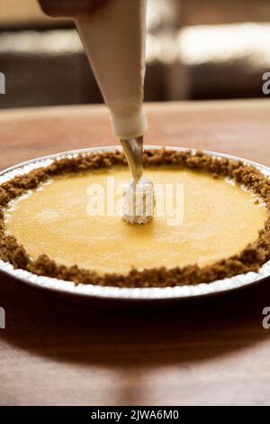 Frau, die einen Käsekuchen vorbereitet. Sie setzt Creme darauf, um ihr den letzten Schliff zu geben. Bereit, es in ihrem Restaurant zu verkaufen Stockfoto