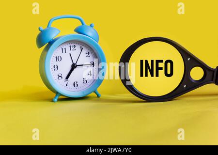 Info-Wort auf einer Lupe auf gelbem Hintergrund mit einer Uhr. Geschäftskonzept. Stockfoto