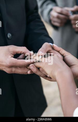 Braut und Bräutigam legen Ringe auf die Finger der anderen während der Hochzeit im Freien. Liebe liegt in der Luft Stockfoto