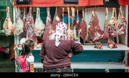 Osch, Kirgisistan - 2022. Mai: Unbekannte Frau untersucht eine Vielzahl von Fleisch unter freiem Himmel in einer Metzgerei auf dem lokalen Markt Stockfoto