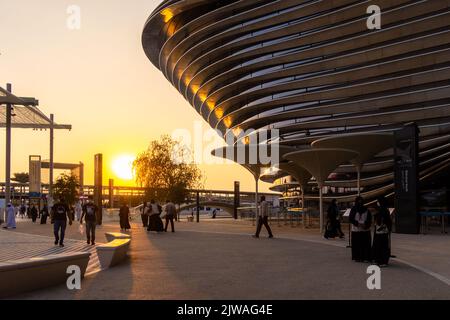 VAE, Dubai - 30. November 2021: Ausstellung EXPO 2020. Menschen gehen zwischen Pavillons entlang. Ausstellungshalle Mobilität in den Abendstrahlen des Sonnenuntergangs. Stockfoto