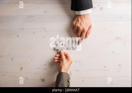 Männliche und weibliche Hand, die zwei leere, passende Puzzleteile auf weißem texturierten Holzhintergrund platziert. Stockfoto