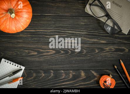 Halloween Hintergrund, Draufsicht. Kürbis und Schulbedarf auf dunklem Holztisch, flach liegend. Rahmen von Halloween orange Lebensmittel, Gläser und Notizblock auf Woo Stockfoto