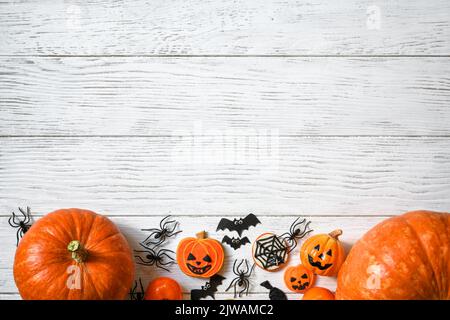 Halloween Hintergrund, Draufsicht. Kürbisse und Süßigkeiten auf weißem Holztisch, flach liegend. Halloween Essen und Dekorationen auf Holzplanken mit Platz. Design, Stockfoto