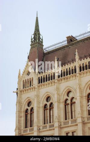 Dies ist ein Teil des Parlamentshauses in Budapest, Ungarn. Sie sehen einen hohen Turm und viele runde und gewölbte Fenster mit einem roten Dach. Stockfoto