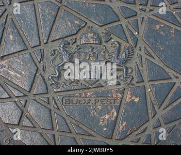 Sehen Sie die Nahaufnahme einer Kanallukenabdeckung auf der Straße in Budapest, Ungarn. BUDA.PEST hat eine Zeit, um zwei Städte zu zeigen. Siehe das Symbol des Wappens. Stockfoto