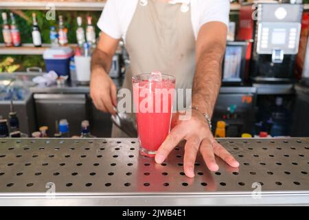Barkeeper serviert frischen roten, violetten Sommerfrucht-Cocktail mit Eis an der Theke an einem sonnigen Tag. Ausgewählter Fokus, geringe Schärfentiefe. Stockfoto
