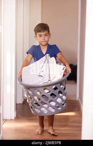 Hilfe rund um das Haus. Porträt eines kleinen Jungen, der einen Wäschekorb mit nach Hause hält. Stockfoto