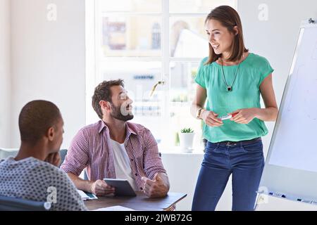 Sie wird immer versuchen, Ihre Fragen zu beantworten. Eine junge Geschäftsfrau, die ihrem Designteam eine Präsentation gibt. Stockfoto