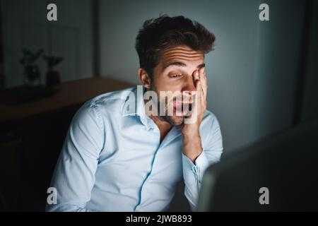 Muss... bleiben... wach... ein junger Geschäftsmann gähnt, während er spät in einem Büro arbeitet. Stockfoto