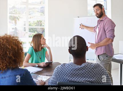 Schauen Sie hier für eine Sekunde nach. Ein junger Geschäftsmann, der seinem Designteam eine Präsentation gibt. Stockfoto
