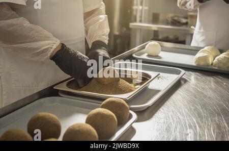 Ein Bauer in schwarzen Handschuhen streut schwarzen Pfeffer auf eine Käsebulle. Der Herstellungsprozess von würzigem Belper knolle Käse Stockfoto