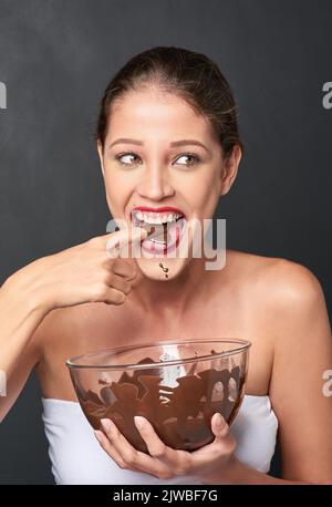 Shes ein Liebhaber von Schokolade. Studioaufnahme einer attraktiven jungen Frau, die von etwas Süßem verlockt wird. Stockfoto