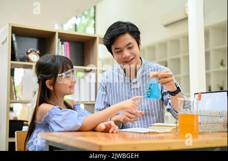 Hübscher asiatischer Lehrer, der einem jungen Schüler im Schülerlabor ein wissenschaftliches Experiment zeigt und lehrt. Stockfoto