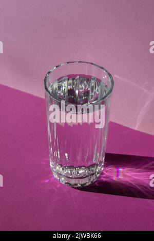 Hochwertige fotokreative, diagonale, isometrische Projektion, Standzeit von Glas Wasser auf violettem Hintergrund. Platz für Text kopieren. Flüssiges alkoholisches Cocktail-Getränk Stockfoto