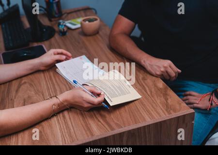 Hände eines Reisebüros, das einen Verkauf macht. Zwei Personen, die einen Vertrag an einem Schreibtisch ausfüllten. Hochwertige Fotos Stockfoto