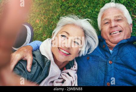 Retirementtime, um Ihr Selfie zu genießen. Ein Seniorenpaar, das sich auf dem Gras legt und ein Selfie macht. Stockfoto