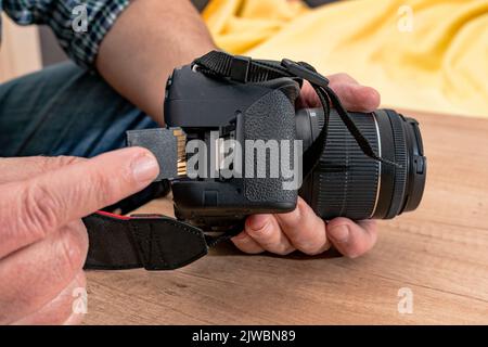 Männlicher Fotograf, der eine Flash-Speicherkarte einsteckt, während er eine professionelle Kamera hält. Stockfoto