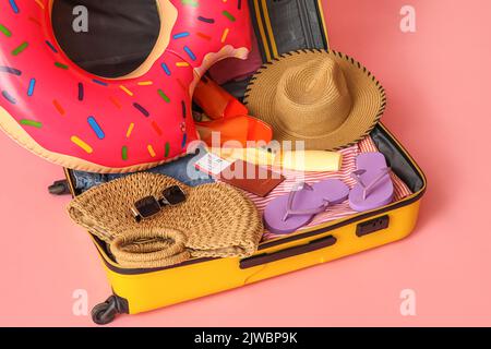 Koffer mit Kleidung, Strandzubehör und Reisepass auf rosa Hintergrund öffnen, Nahaufnahme Stockfoto