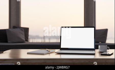 Moderner Heimarbeitsplatz mit tragbarem Laptop-Modell mit weißem Bildschirm, spiralförmigem Notizblock, Kaffeetasse auf dem Tisch über verschwommenem Wohnzimmerhintergrund. Stockfoto