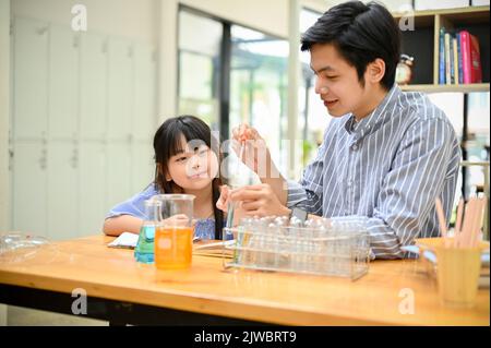 Ein glückliches und süßes junges asiatisches Mädchen konzentriert sich auf das Studium der Wissenschaft, während ihre Lehrerin die chemische Flüssigkeit im Reagenzglas zeigt. Science-Class-Konzept Stockfoto