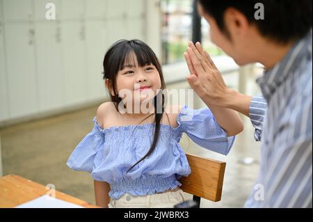 Schönes und lächelndes junges asiatisches Mädchen, das mit ihrem Vater High-five gab, nachdem es einen Deal gemacht hatte. Stolzer Vater mit fünf High-Five und ihrer Tochter. Stockfoto